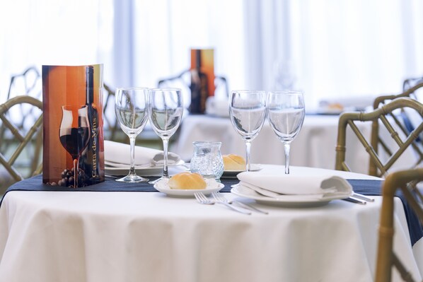Una mesa de comedor dispuesta con copas de vino, platos y una carta.