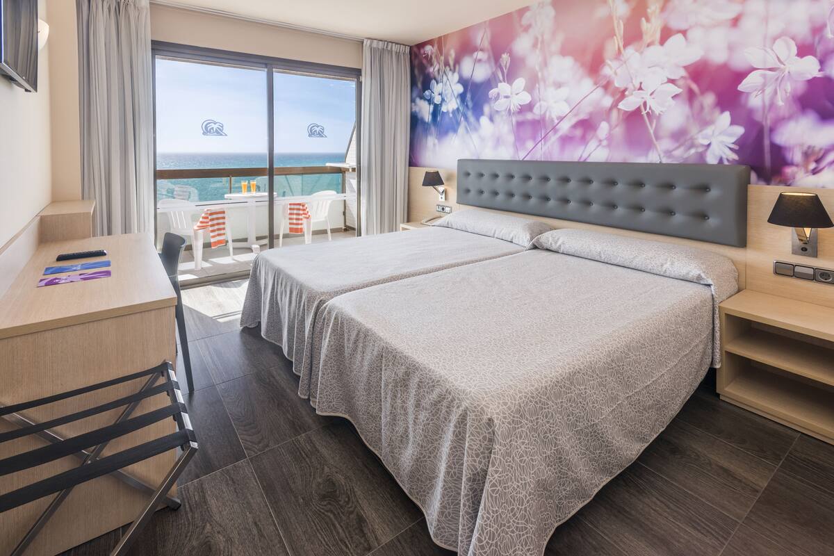 Ett hotellrum med två sängar, ett skrivbord och en balkong med utsikt över havet.