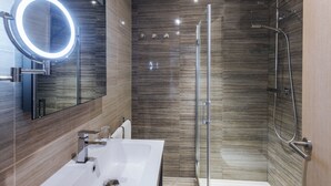 Un baño moderno con un lavamanos blanco, un espejo redondo con luz y una ducha con cerramiento de vidrio.