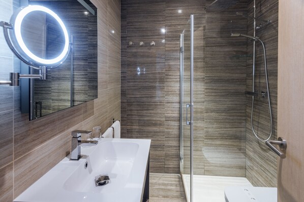 A modern bathroom with a white sink, a round mirror with a light, and a glass-enclosed shower. - Hotel Tropic Park (Malgrat de Mar)