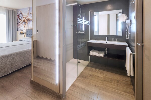 Une chambre d’hôtel moderne comprenant un lit, une douche en verre, une salle de bain avec un lavabo et un miroir, et une grande œuvre d’art accrochée au mur.
