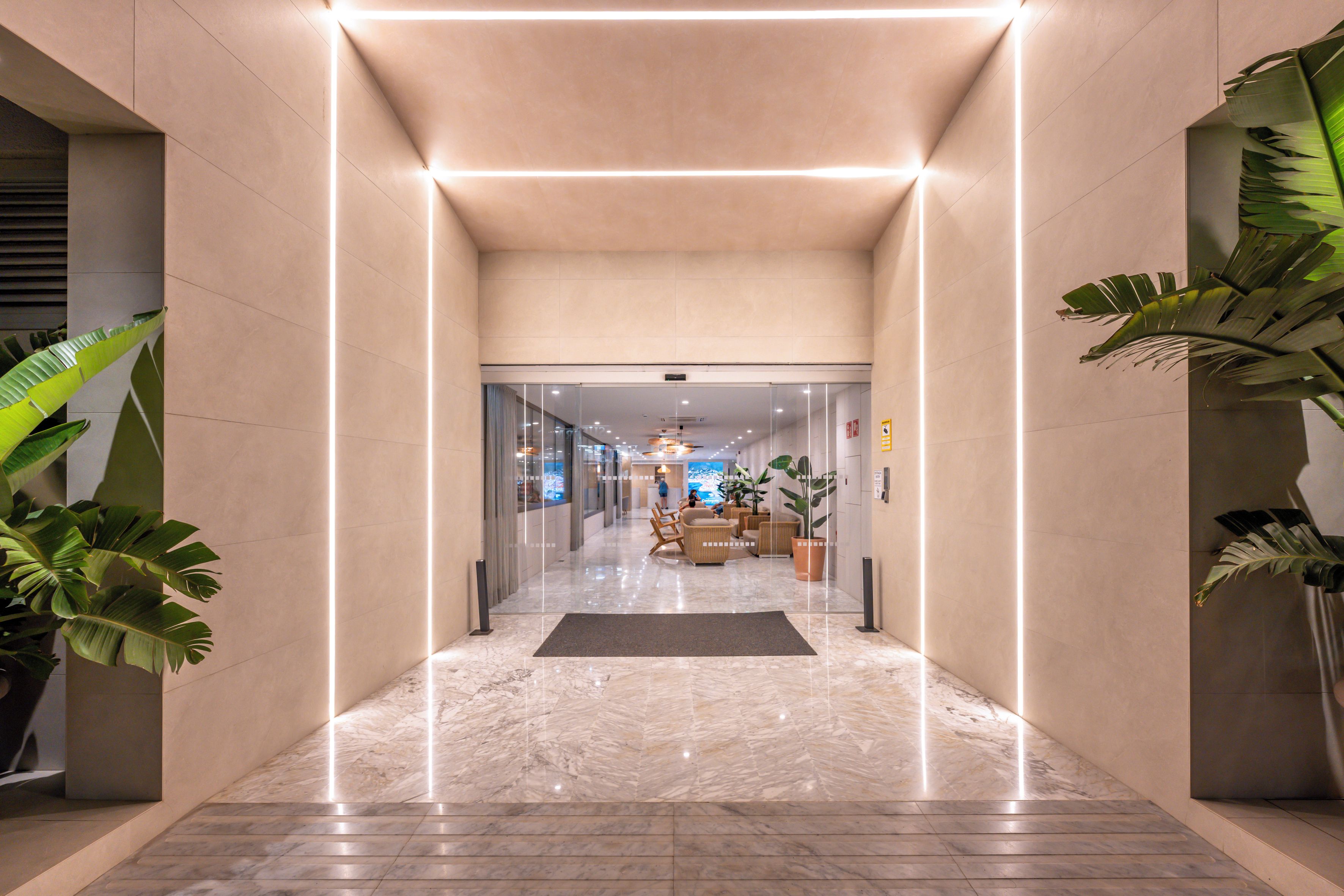 Un hall d’hôtel moderne avec un sol en marbre, des portes en verre et des plantes en pot.