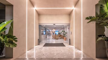 En modern hotellobby med ett marmorgolv, glasdörrar och krukväxter.