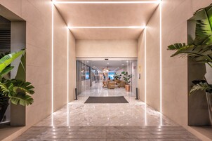 Un moderno vestíbulo de hotel con piso de mármol, puertas de cristal y plantas en macetas.