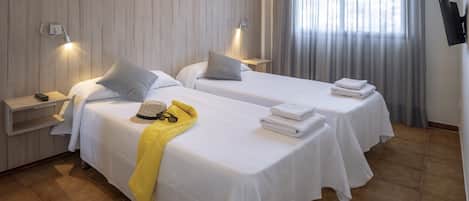 Habitación de hotel con dos camas, un televisor, un escritorio y una ventana con cortinas.