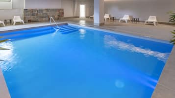 An indoor swimming pool with clear water, a diving board, and several white lounge chairs around the pool area.