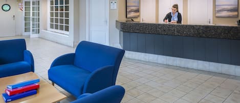 Un área de recepción con una recepcionista, sillas azules, un mostrador y vistas al exterior.