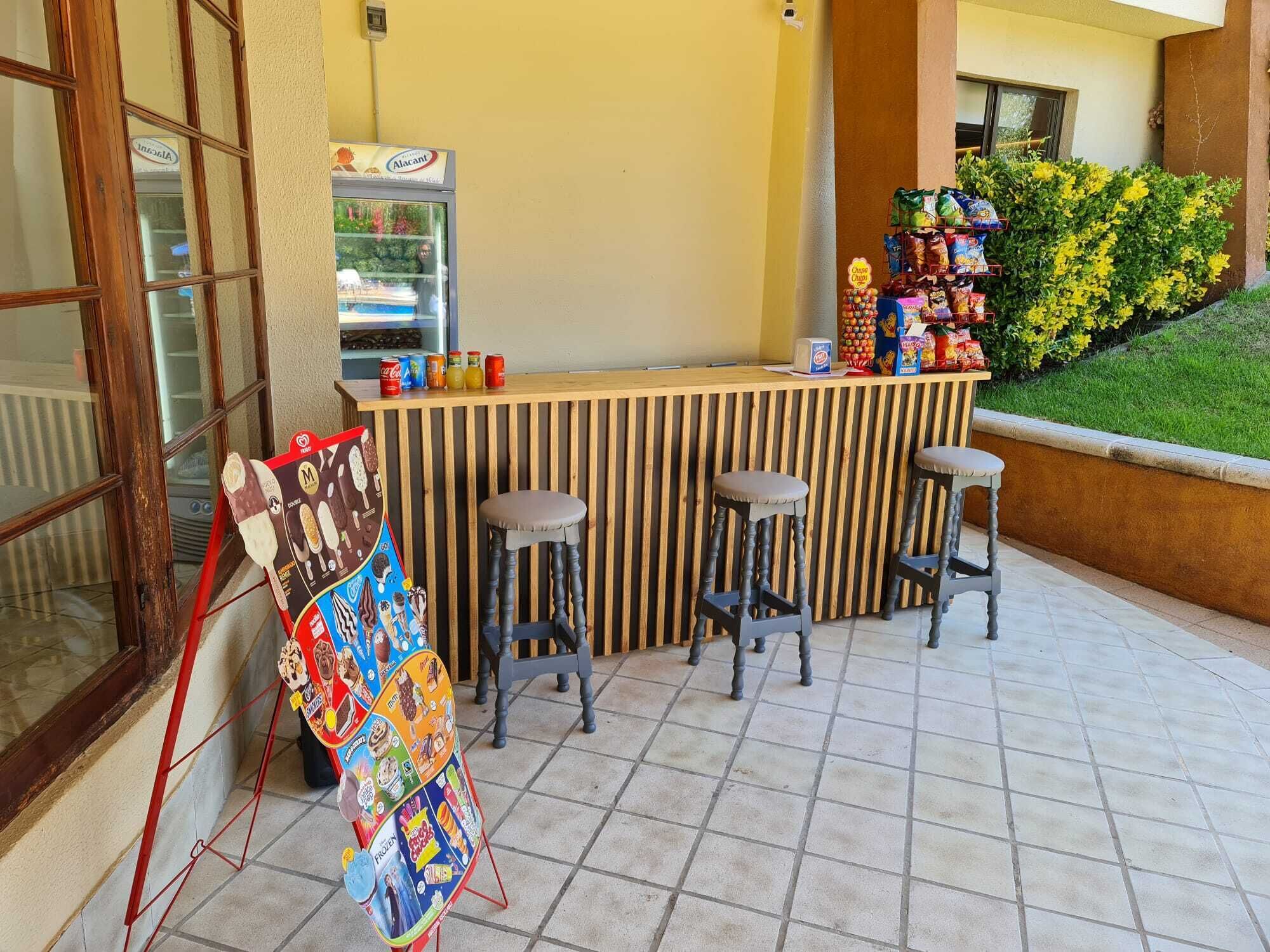 An outdoor bar area with a counter, stools, and a display of snacks and beverages.