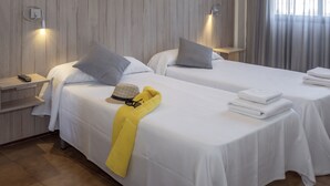 A hotel room with two beds, each with white linens and pillows, a bedside table with a remote control, and a yellow towel on one bed. - Apart-hotel GHT Tossa Park (Tossa de Mar)