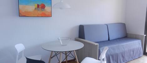 A small room with a blue sofa, a white table with a glass, and two chairs.