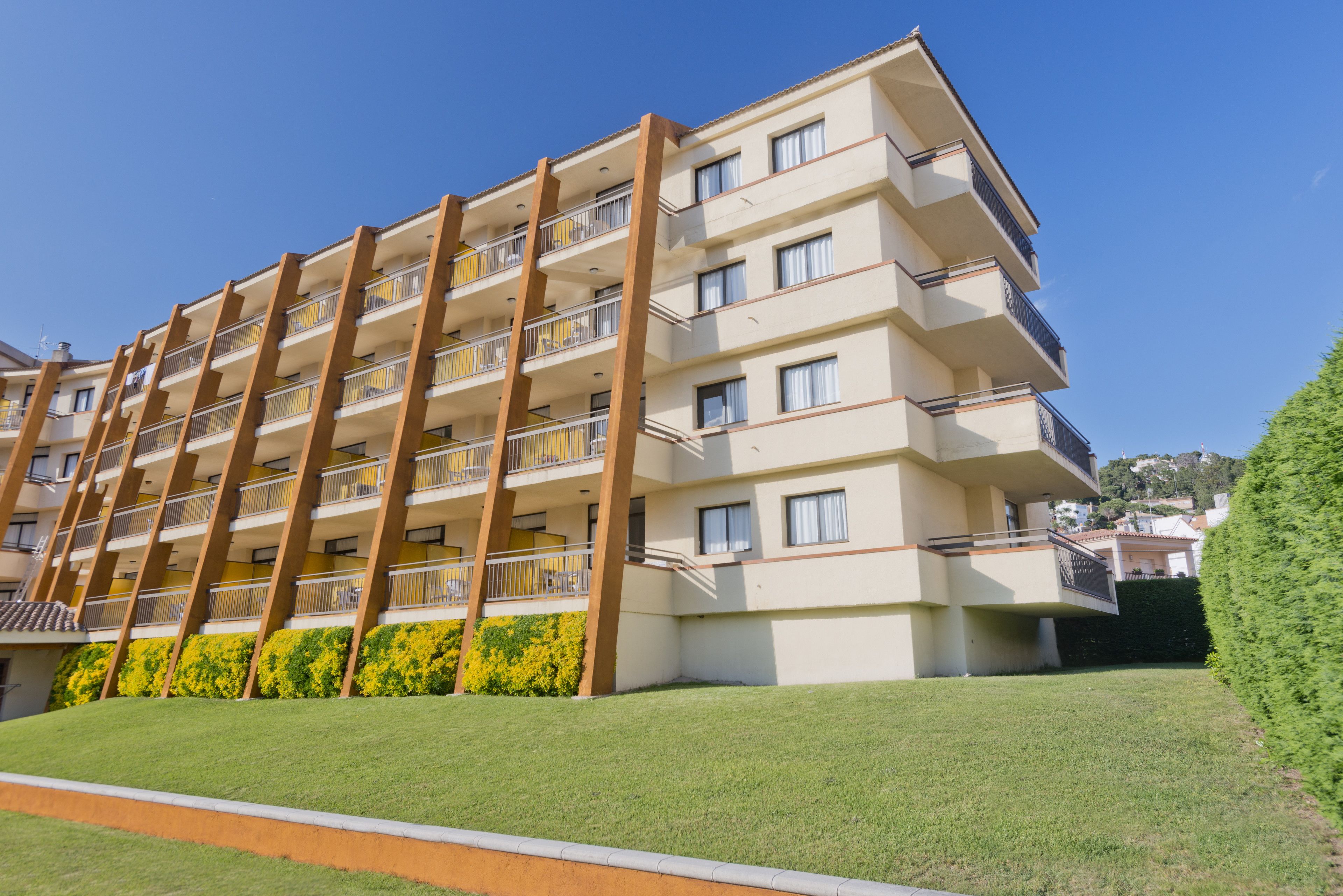 Un hôtel à plusieurs étages doté de balcons, d’une pelouse bien entretenue et surplombant un ciel bleu dégagé.