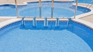 A swimming pool with clear blue water, tiled edges, and metal pool ladders. - Apart-hotel GHT Tossa Park (Tossa de Mar)