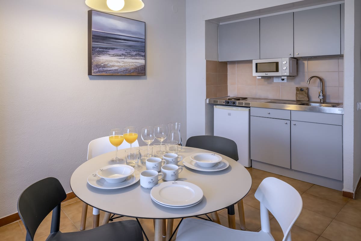 Uma cozinha moderna com micro-ondas, pia e armários. Uma mesa de jantar com pratos, copos e um quadro na parede.