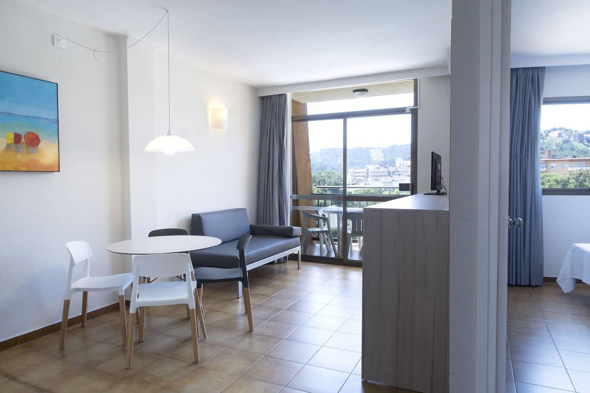 Quarto de hotel moderno com área de refeições, um sofá e uma TV.