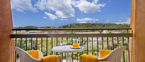 A balcony with two white chairs, a small round table, and a yellow towel on each chair.
