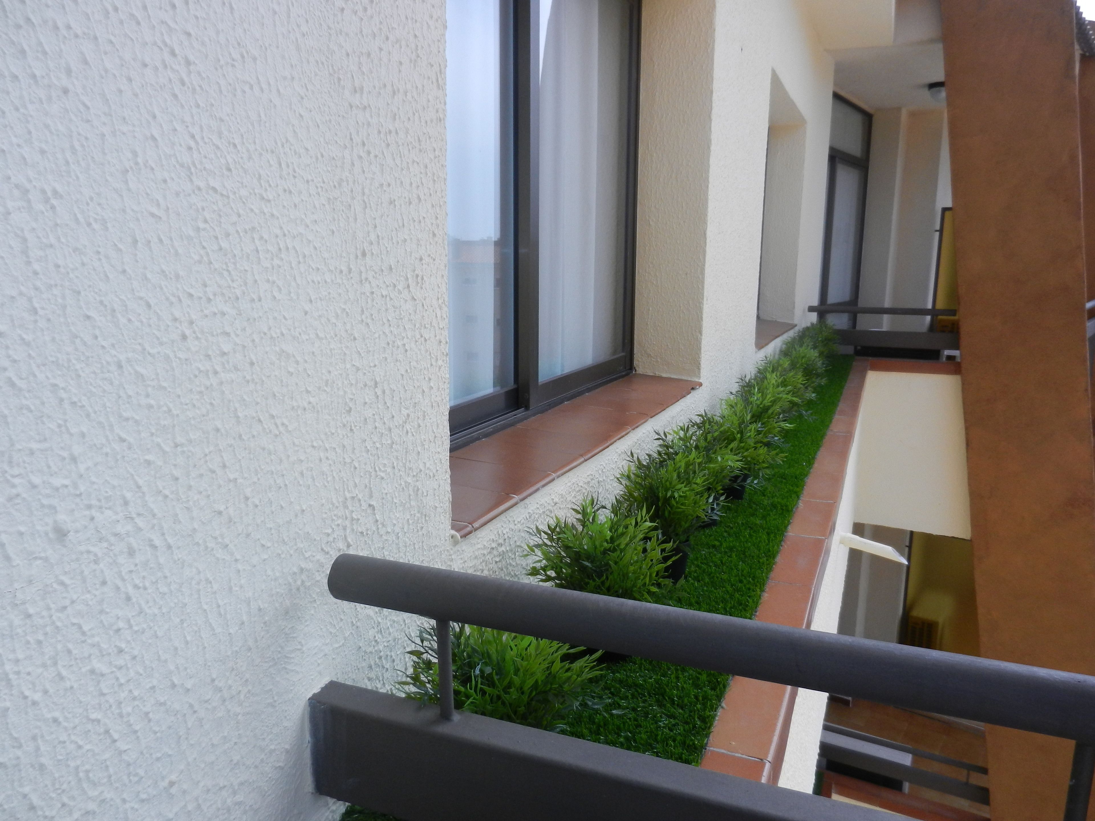 Un edificio moderno con balcón, puerta de vidrio y un pequeño jardín.