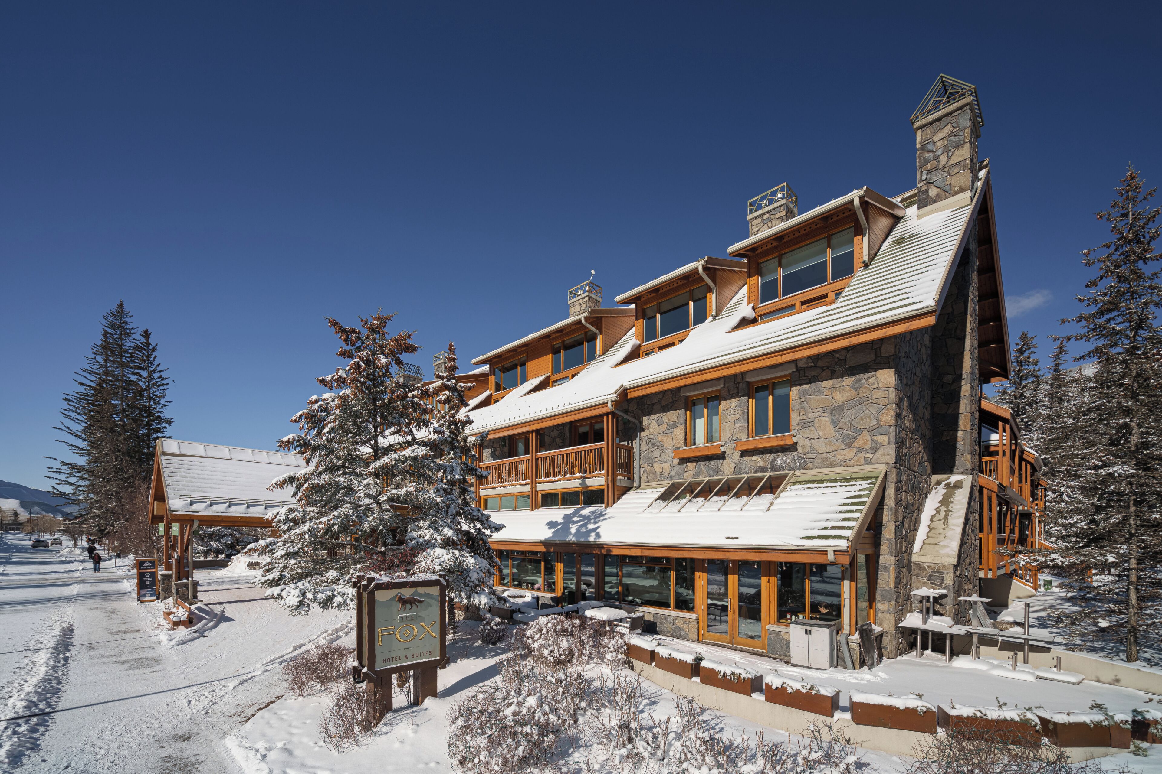 A large, multi-story hotel with a stone facade and wooden accents, featuring a prominent sign for 'The Fox Hotel & Suites' in a snowy landscape.