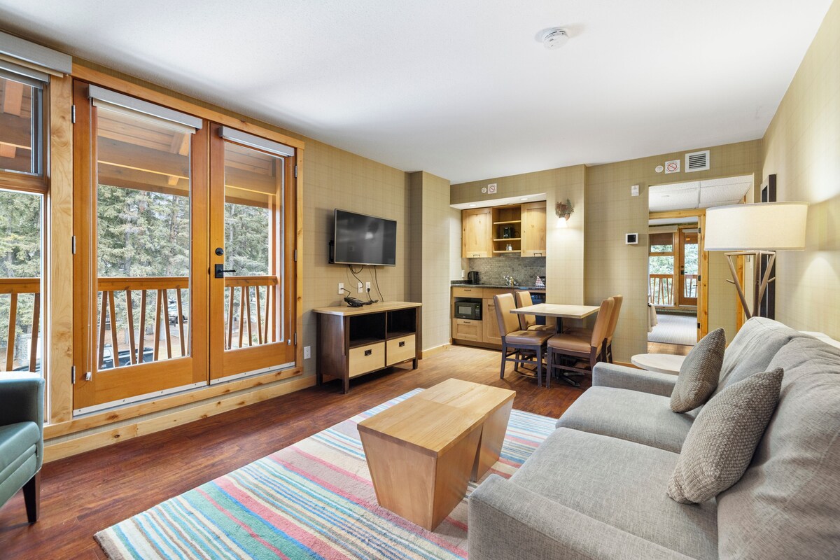 A spacious living room with a sofa, coffee table, and a TV mounted on the wall.