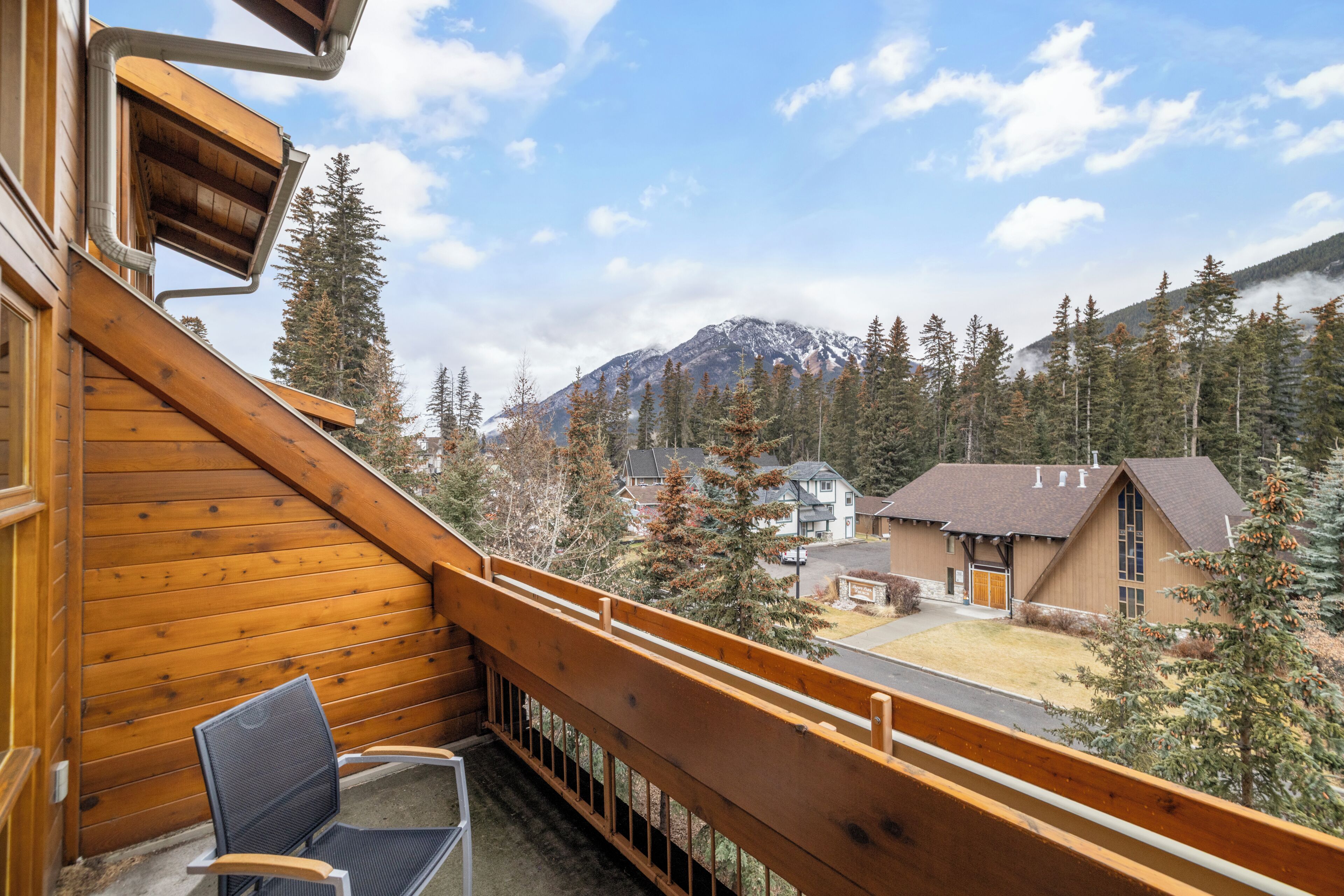 A wooden balcony with a chair, overlooking a mountain and a residential area.