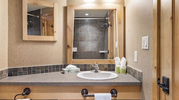 A bathroom with a wooden vanity, a sink, a mirror, and a shower visible through the door.