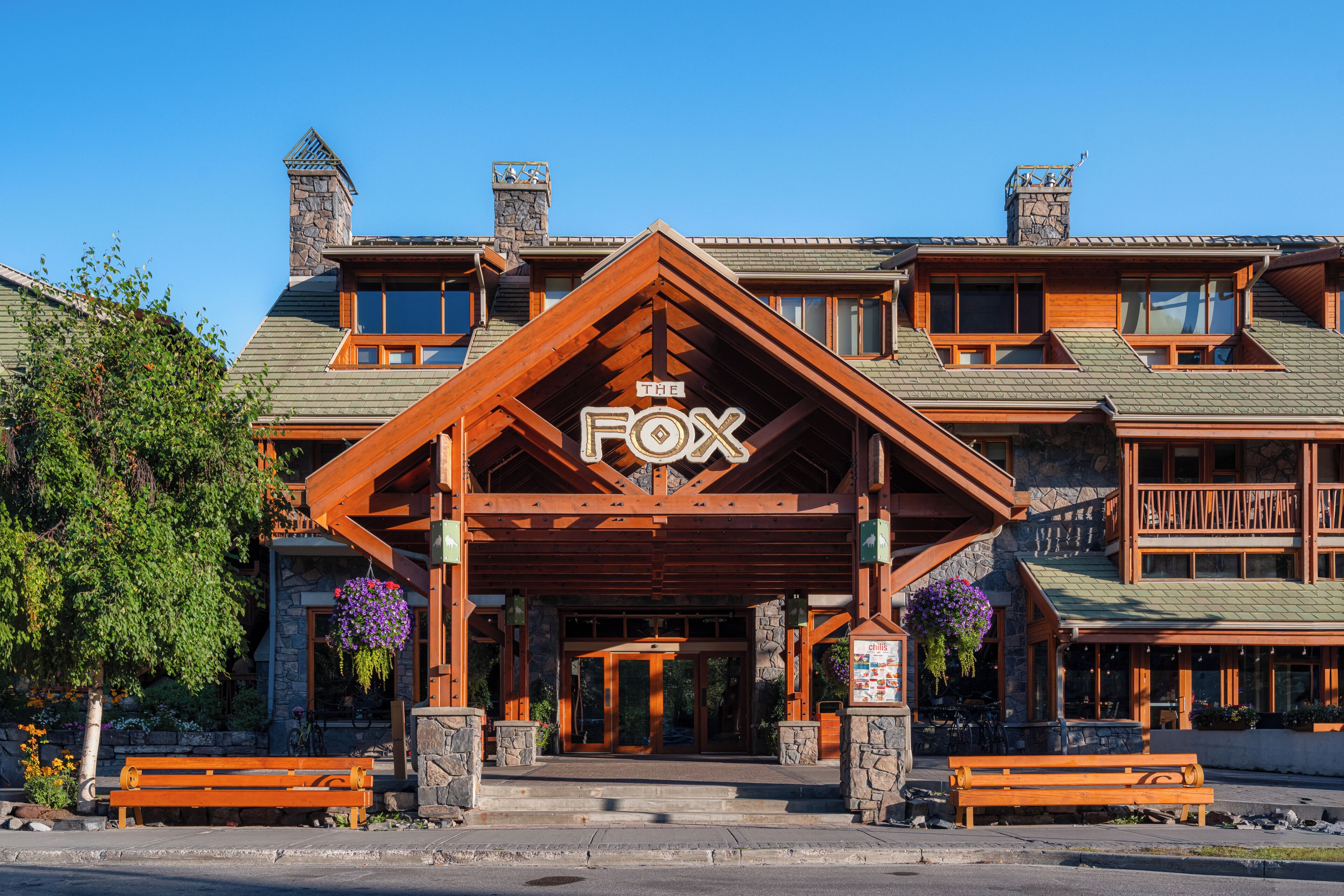 Una cabaña con un llamativo letrero 'FOX', fachada de piedra, balcones de madera y una chimenea de piedra.