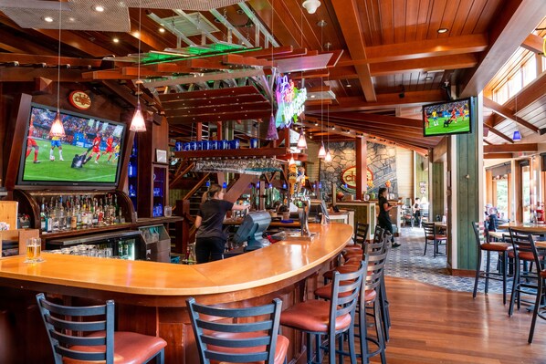 Een bar met een gebogen toonbank, diverse barkrukken en een televisie waarop een sportevenement wordt getoond.