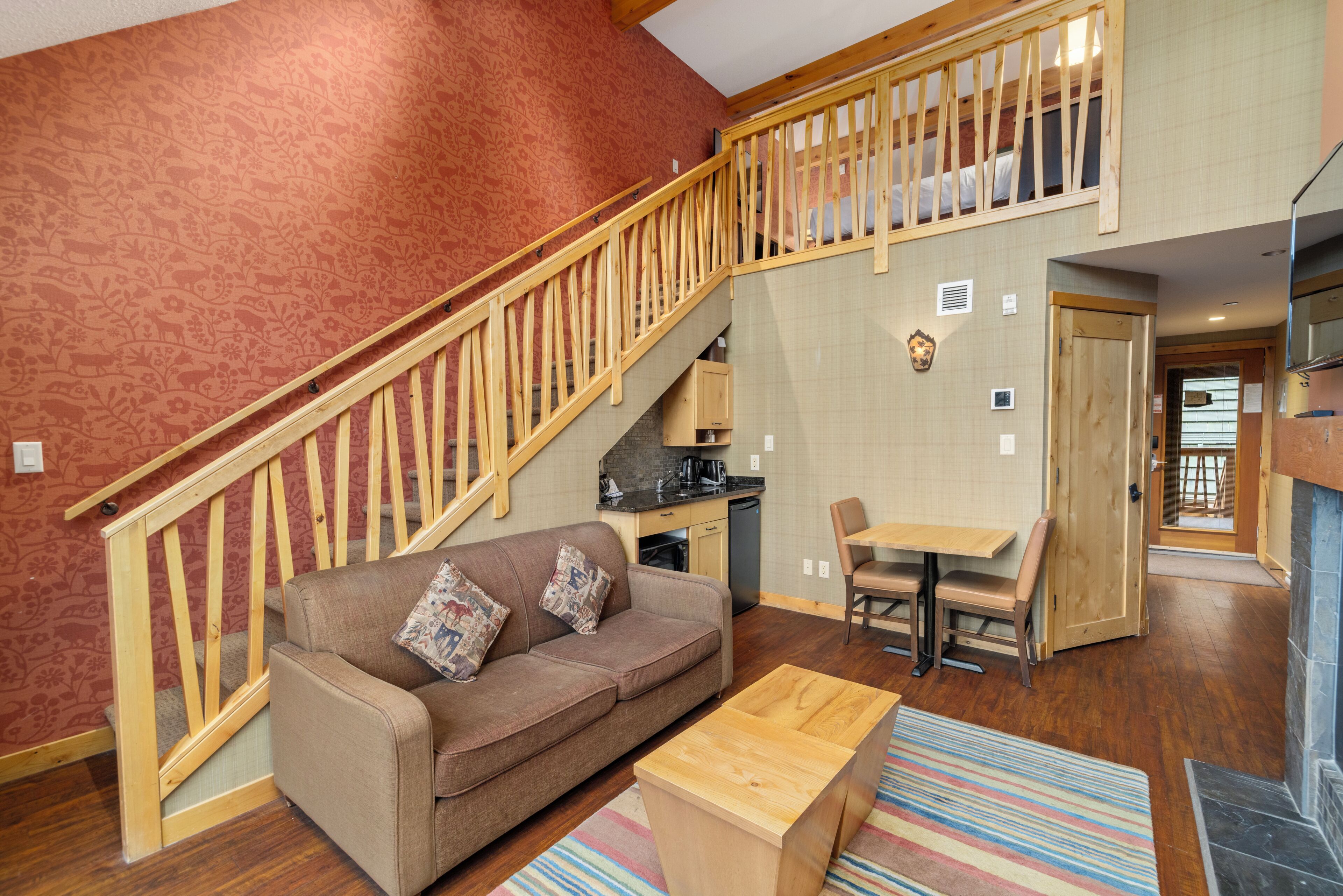 A multi-level living space with a wooden staircase, a sofa, a coffee table, and a kitchen area.