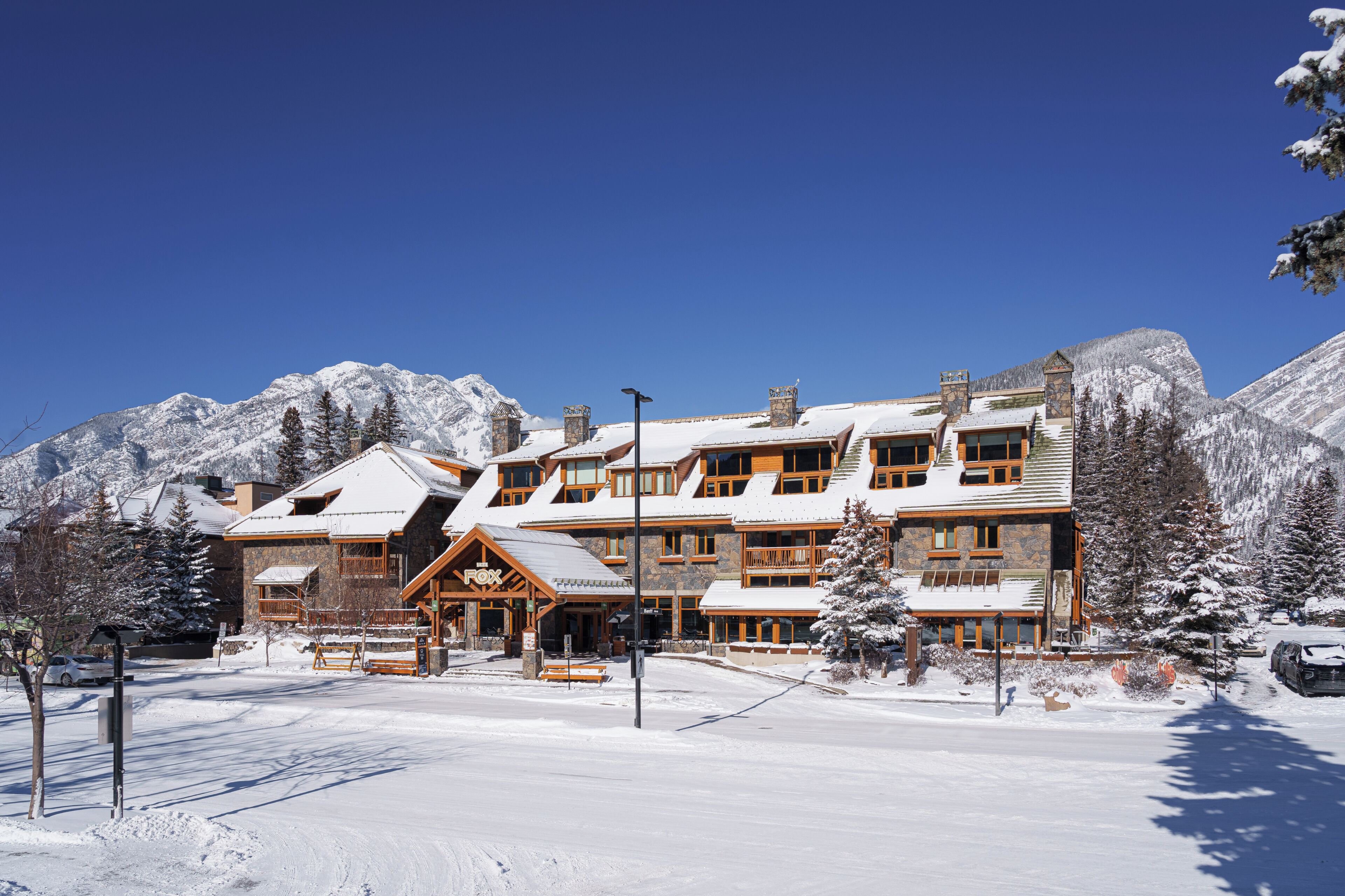 A large, multi-story lodge with a stone facade and wooden accents, surrounded by snow-covered mountains.