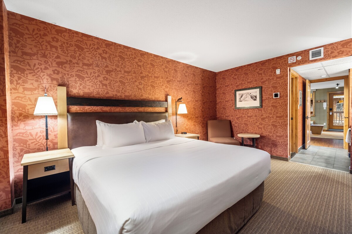 A hotel room with a large bed, two bedside tables with lamps, a chair, and a picture on the wall.