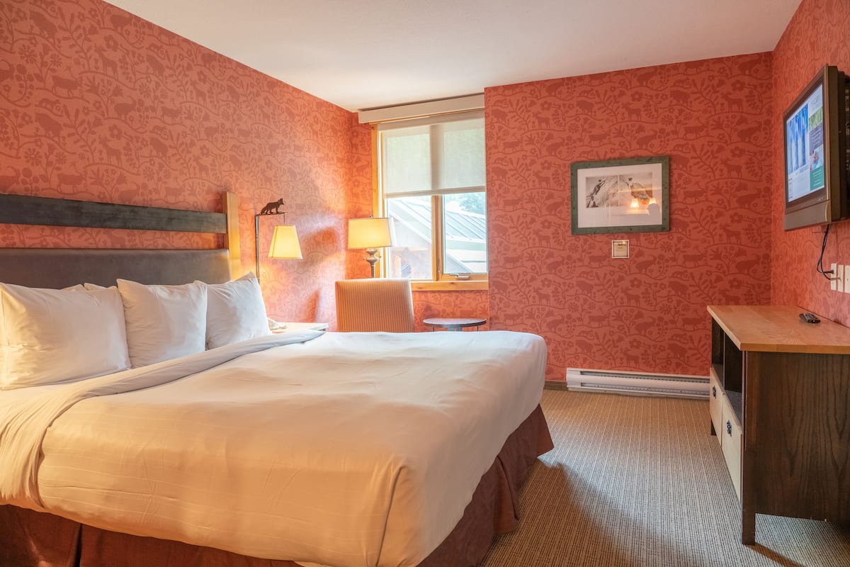 A hotel room with a large bed, a desk, a chair, and a window.