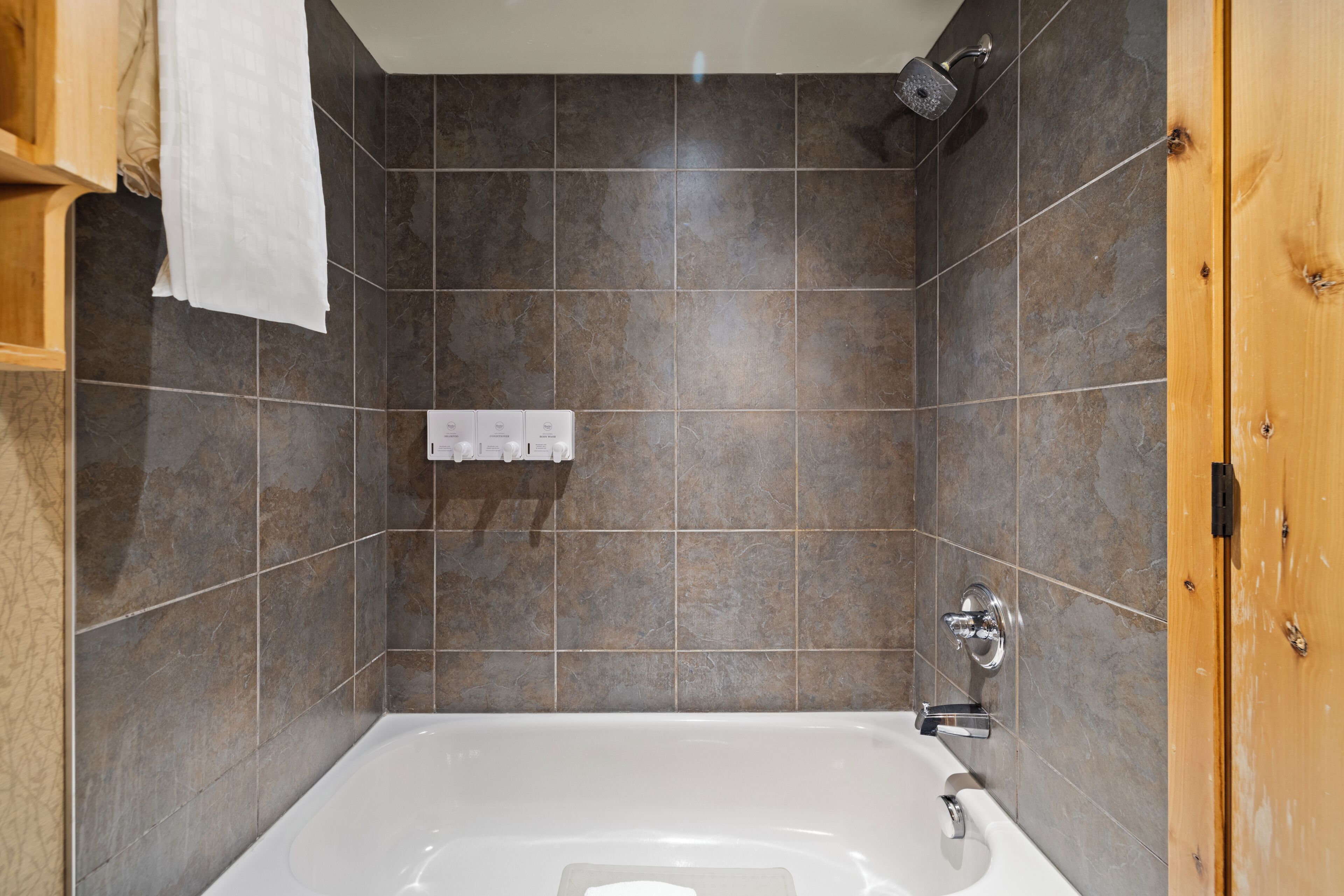 A modern bathroom with a bathtub, a shower, and a wooden door.