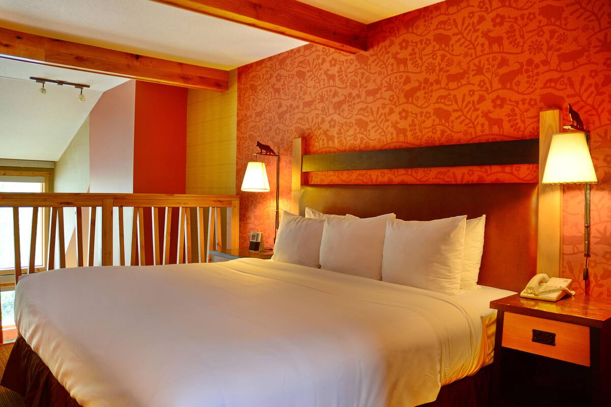 A hotel room with a large bed, wooden headboard, two bedside lamps, a telephone, and a window with a view of the outdoors.