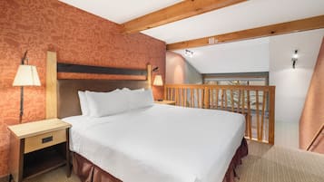 Habitación de hotel con cama, mesitas de noche, lámpara, cabecero de madera, balcón con barandilla y pared con diseño.