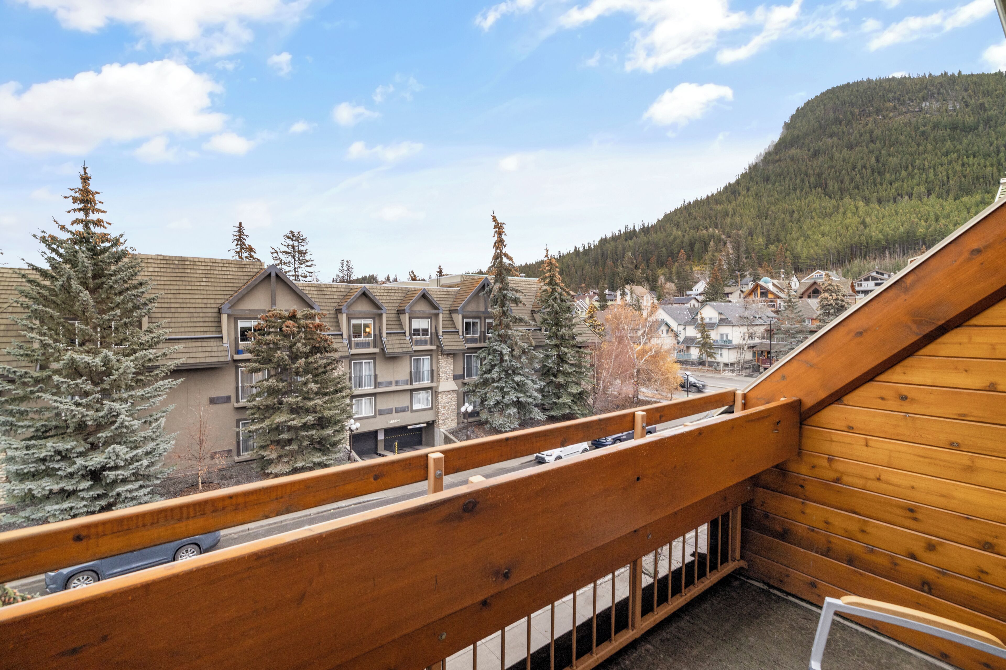 A wooden balcony with a view of a residential area, including houses and a mountain in the background.