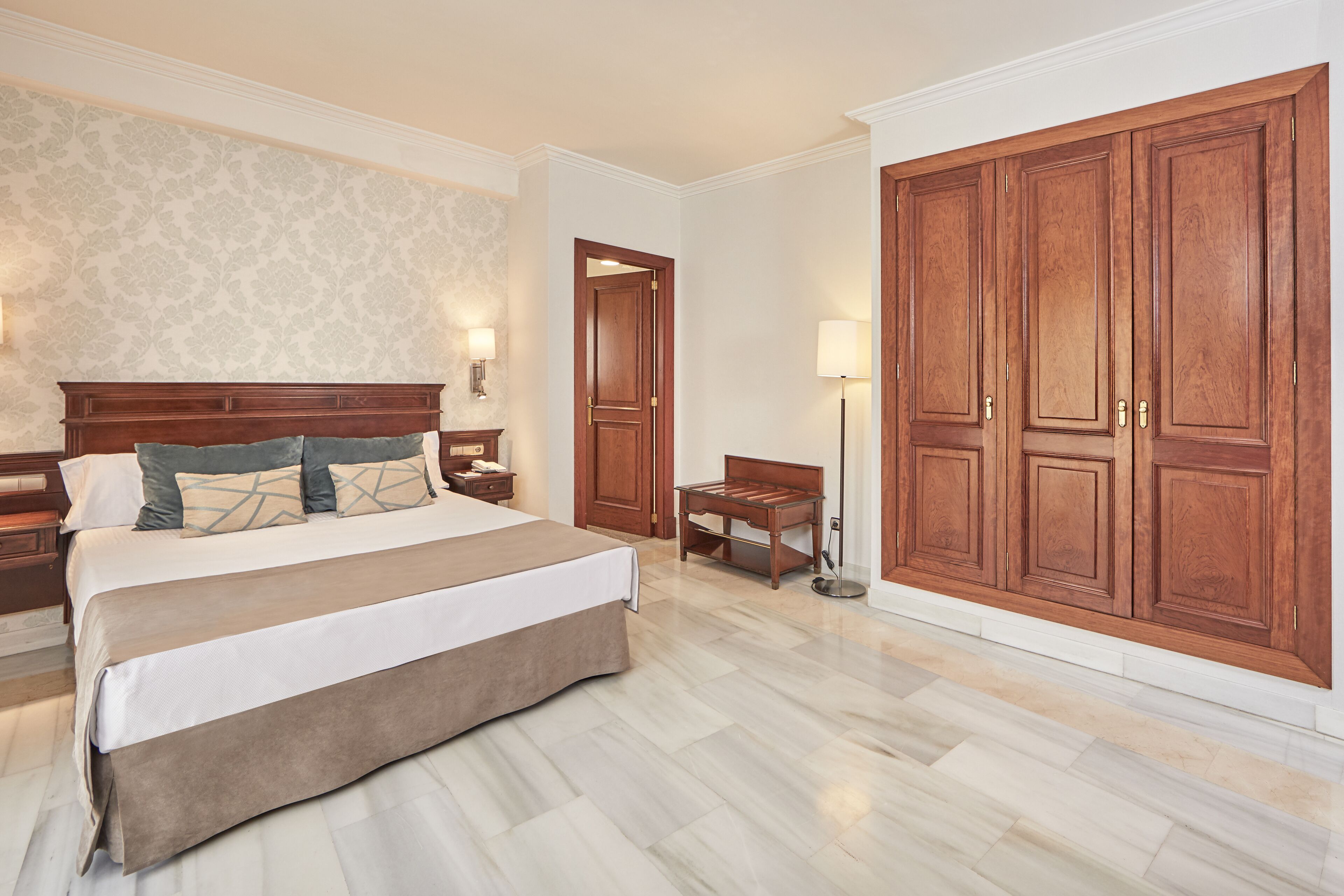 A hotel room with a large bed, wooden wardrobe, and a nightstand with a lamp.