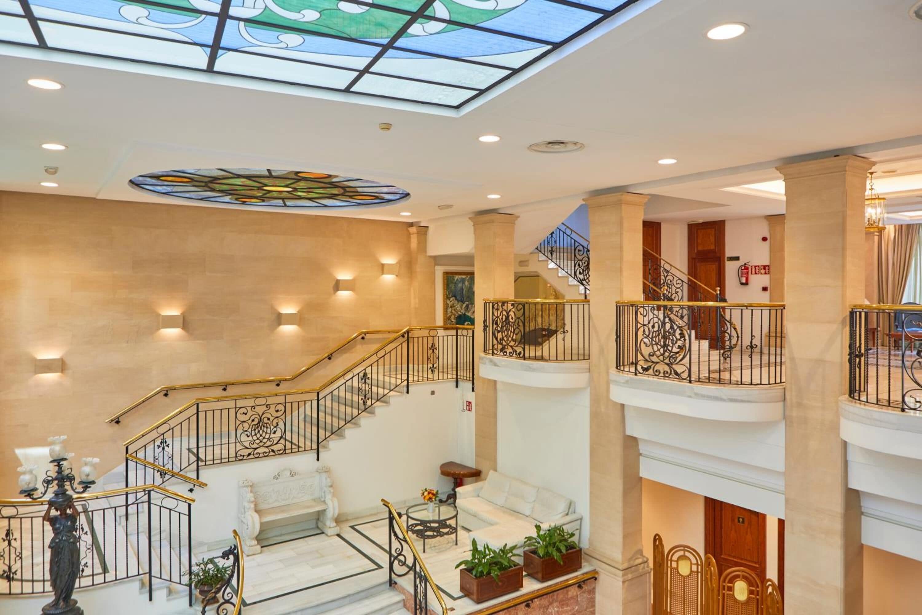 A multi-level hotel lobby with a grand staircase, a seating area, and a decorative ceiling.