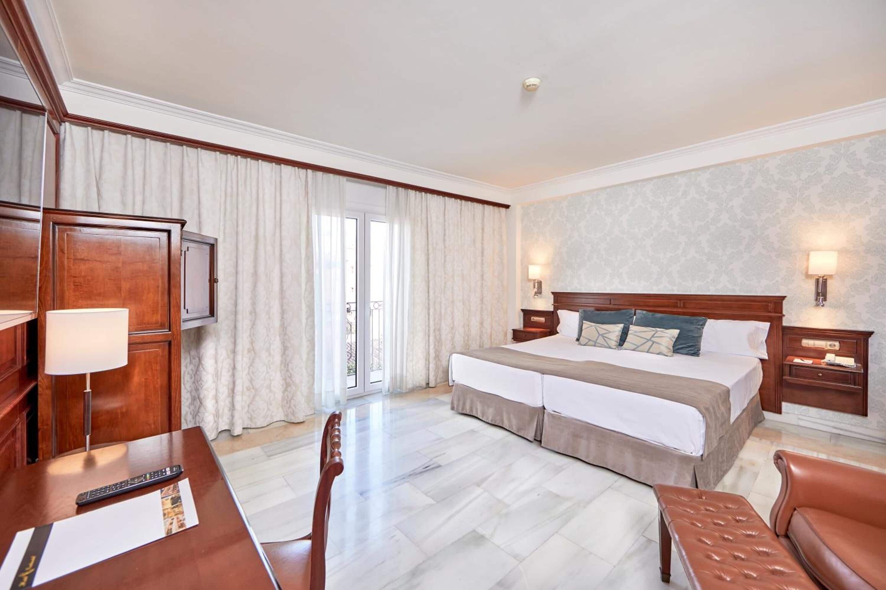 A hotel room with a large bed, a desk with a lamp, a chair, and a TV.
