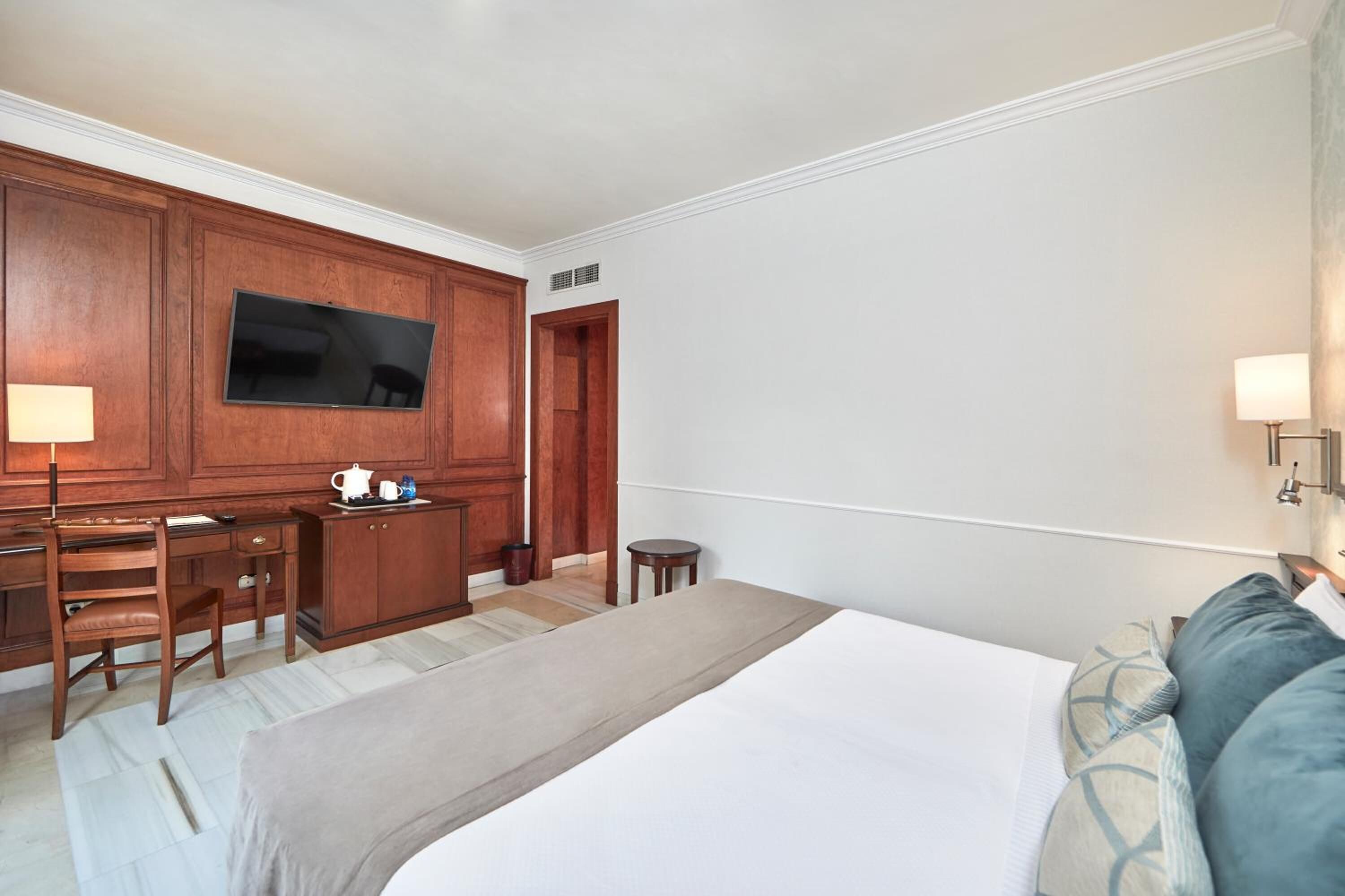 A hotel room with a large bed, a desk with a chair, a television, and a small table.