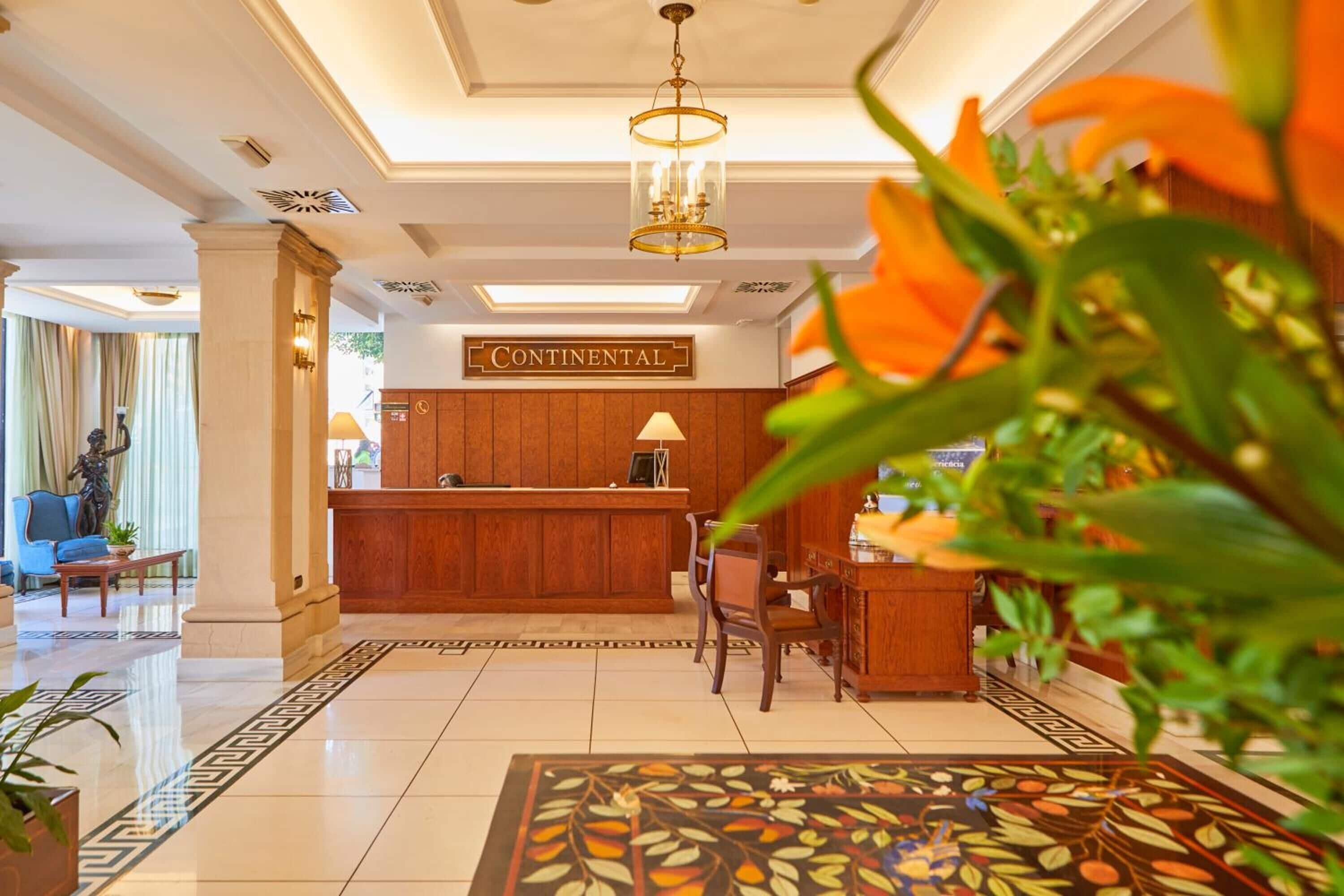 Un hall de hotel con mostrador de recepción, una araña y una alfombra estampada.