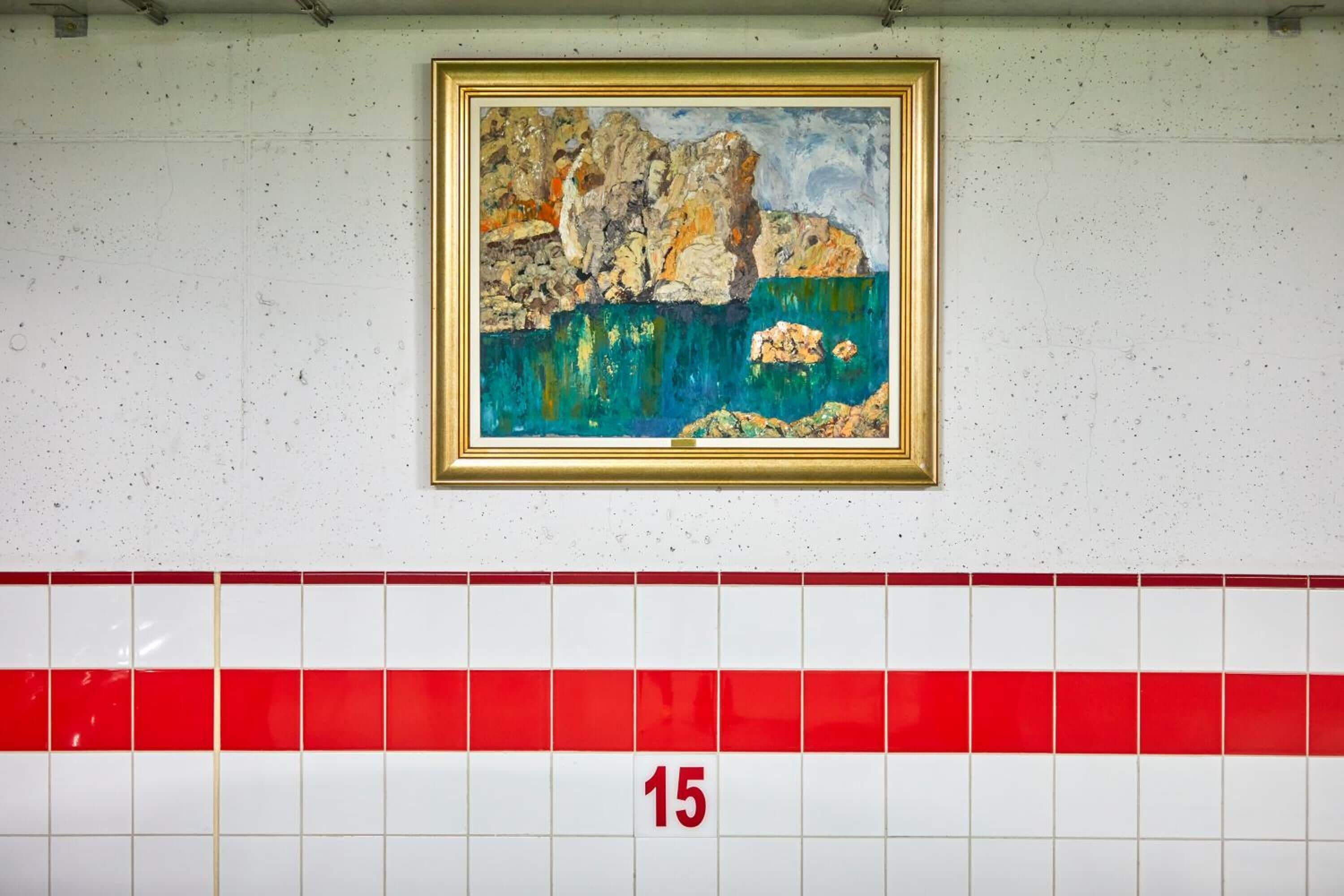 A tiled wall with a framed painting of a rocky landscape and a red and white tiled floor with the number 15.