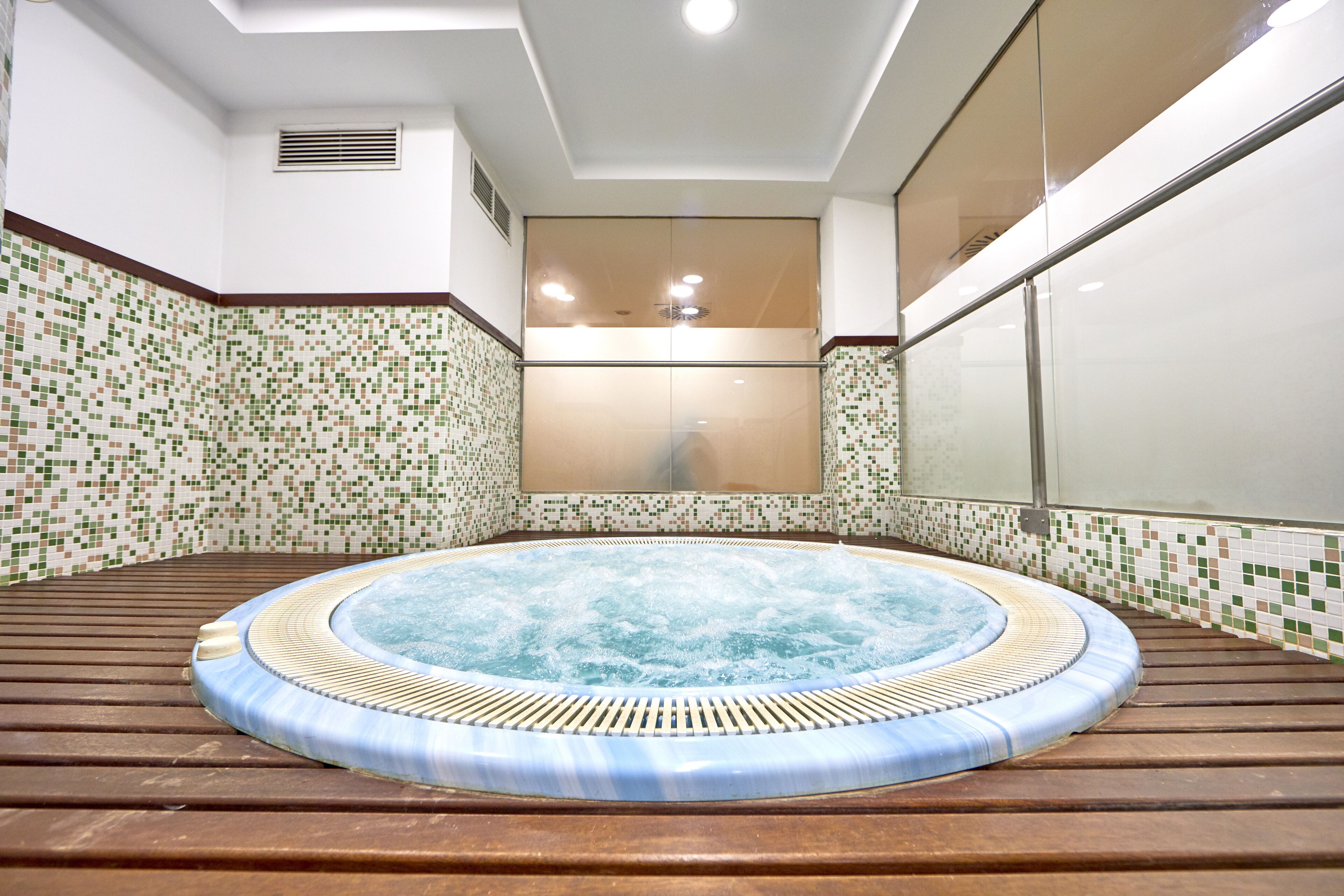 A hot tub in a room with tiled walls and a wooden floor.