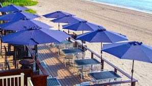 Un patio frente a la playa con sombrillas y asientos, con vista al océano.