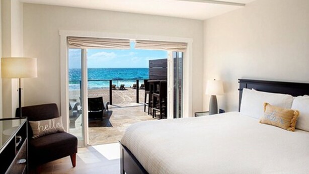 Habitación de hotel con cama, escritorio, silla y vista a la playa y al océano.