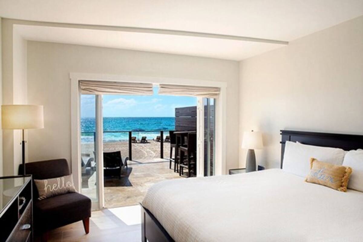 A hotel room with a bed, a desk, a chair, and a view of the beach and ocean.