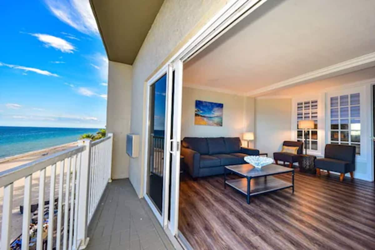 A balcony with a view of the ocean, furnished with a sofa, chairs, and a coffee table.