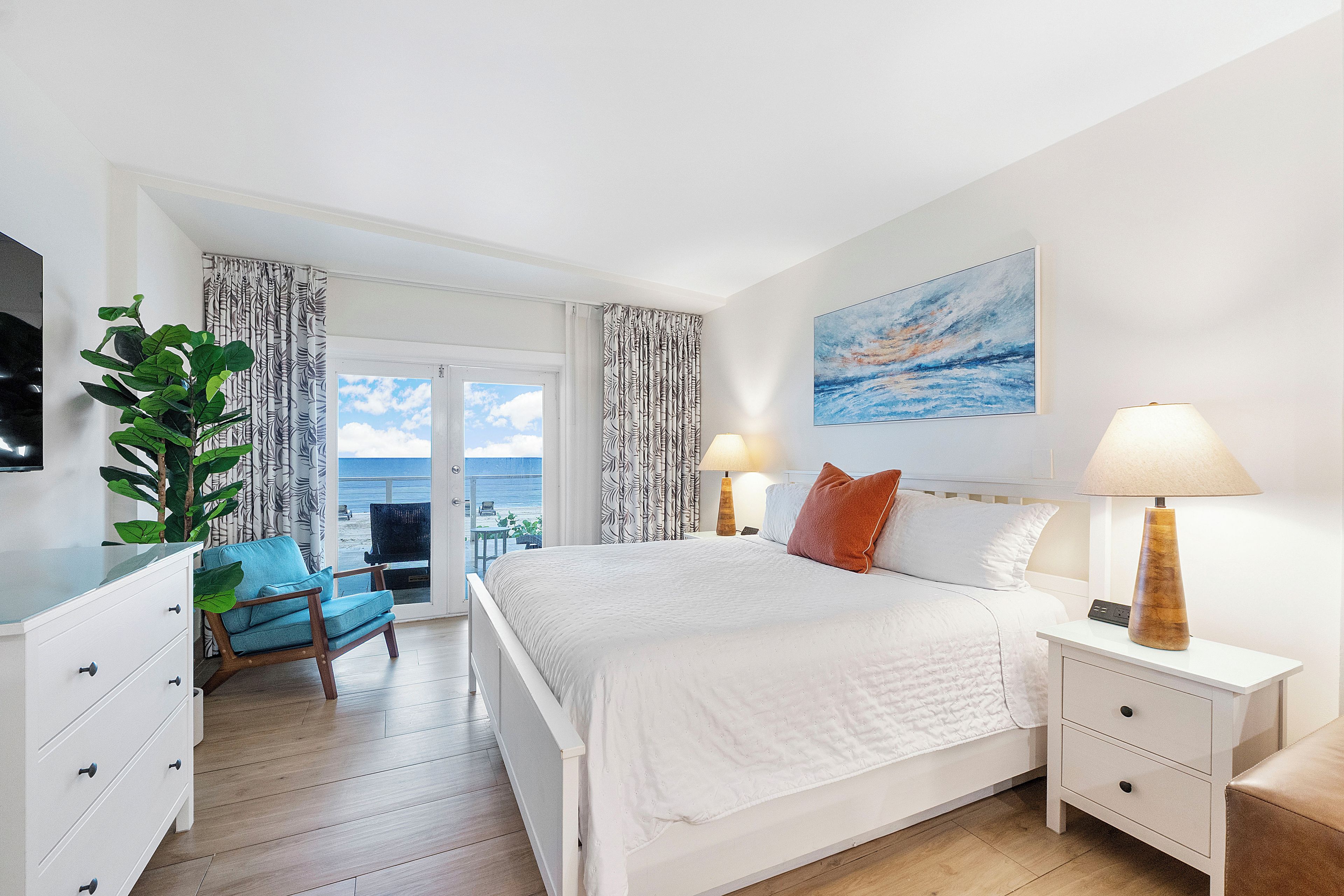 A hotel room with a bed, a desk, a chair, a television, a window with curtains, and a painting on the wall.
