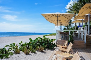 A beachside patio with wooden deck chairs and umbrellas, overlooking the ocean.