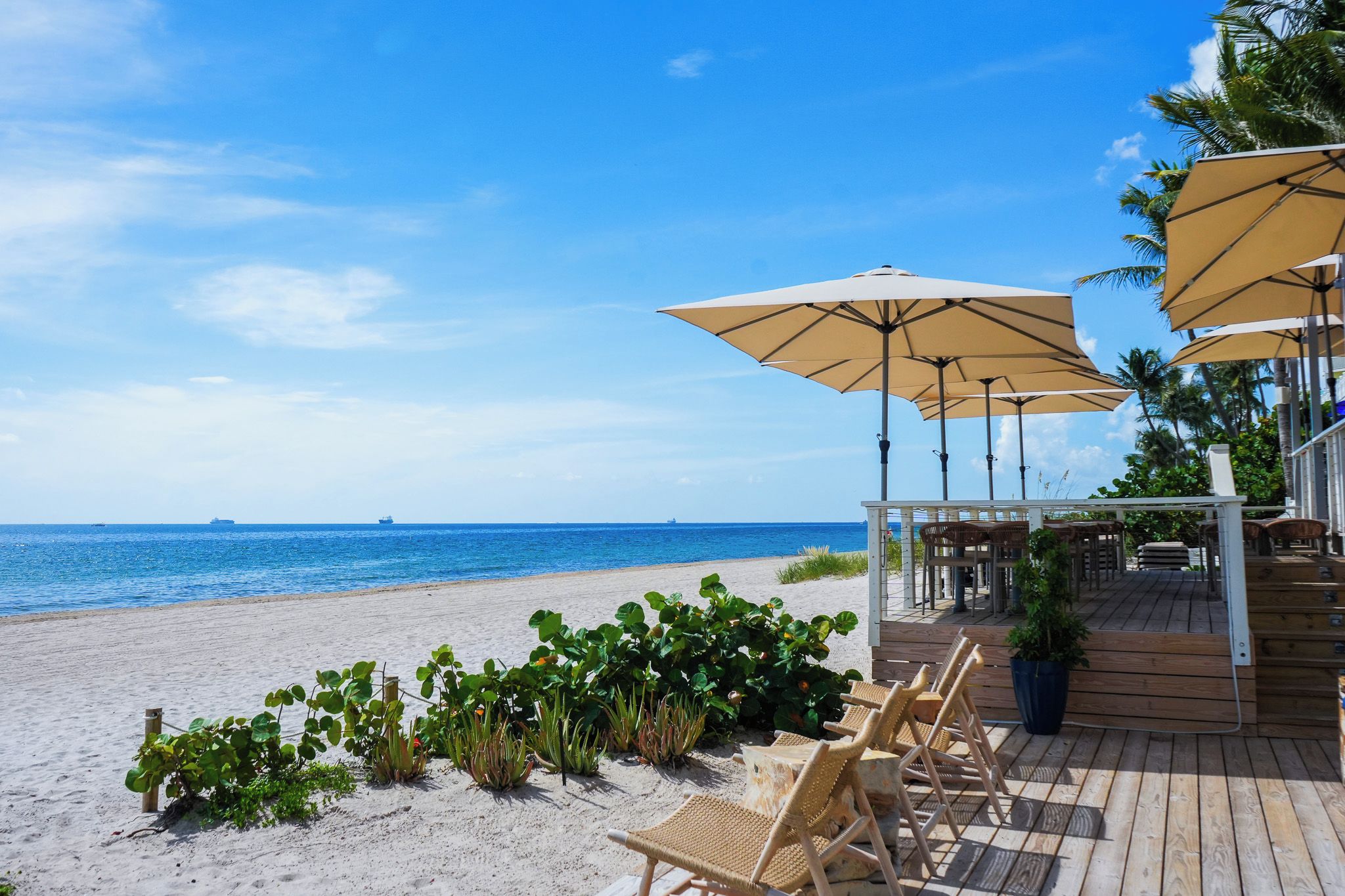 A beachside patio with outdoor seating and umbrellas, overlooking the ocean.