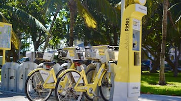 Una estación de alquiler de bicicletas amarillas con un cartel de AvMed Rides, cerca de palmeras y un mapa en el suelo.