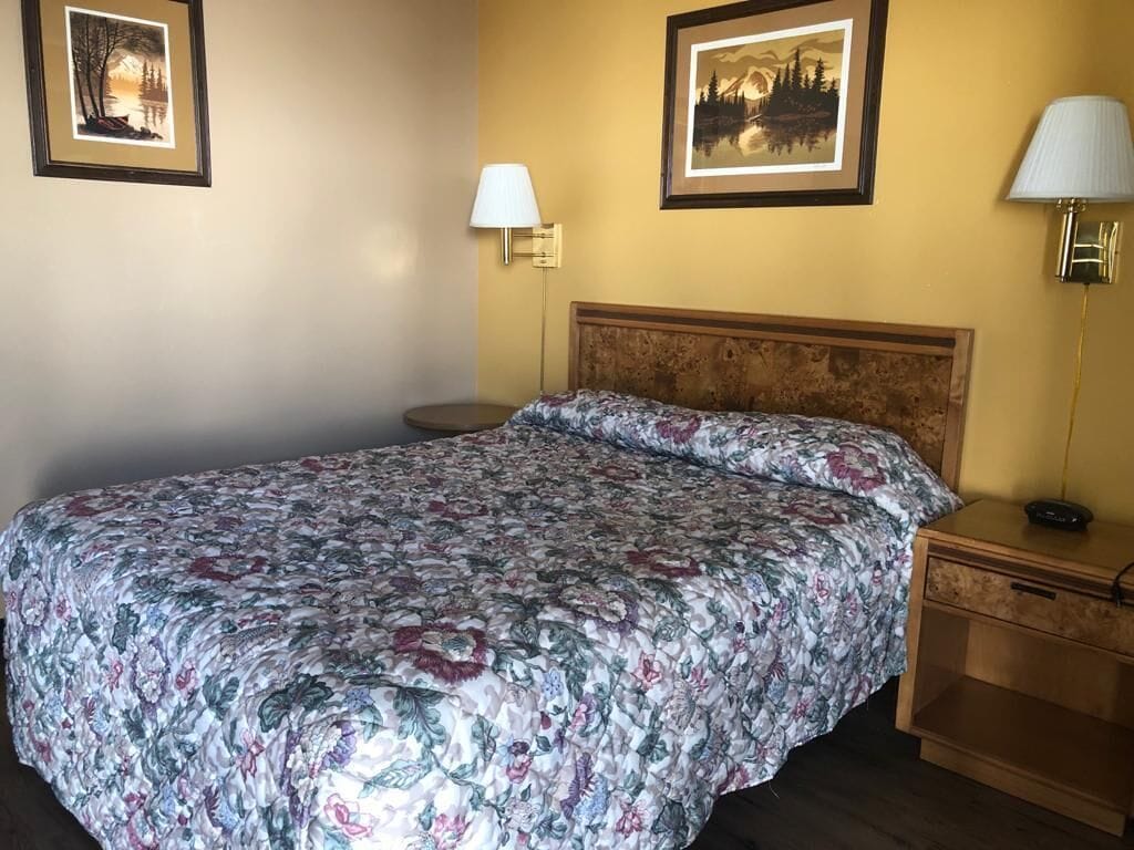 A hotel room with a large bed, two bedside tables, and two wall-mounted lamps.